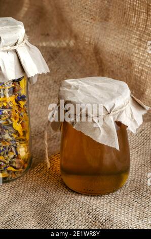 Erbe e medicina alternativa concept.erbe medicinali essiccati erbe e miele di api. Tè di fiori secchi e miele liquido crudo in vasetti di vetro su burlap. Foto Stock