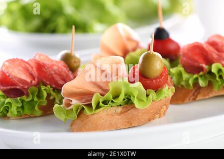 Tartine di baguette tenue con lattuga, salame o prosciutto di Parma, pomodori, mozzarella e olive. Piatto assortito di prelibatezze per la festa. Foto Stock