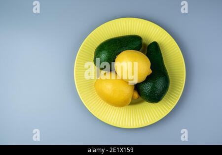 Avocado, limoni in un piatto giallo su sfondo grigio. Vista dall'alto con spazio da copiare. Foto Stock