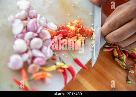 primo piano di un taglio manuale di cipolle bianche e peperoncino pepare su un tavolo da cucina con un coltello Foto Stock