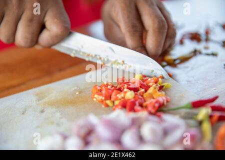 primo piano di un taglio manuale di cipolle bianche e peperoncino pepare su un tavolo da cucina con un coltello Foto Stock