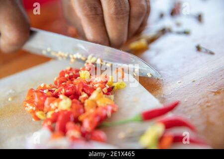 primo piano di un taglio manuale di cipolle bianche e peperoncino pepare su un tavolo da cucina con un coltello Foto Stock