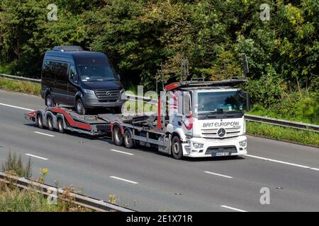 Conducenti di autotrasportatori europei Brit: Veicoli per la consegna camion che trasportano Mercedes Benz sprint su autocarri rimorchio, veicoli per impieghi gravosi, trasporto, camion, veicolo di trasporto di automobile, HGV di industria commerciale europea, M6 a Manchester, Regno Unito Foto Stock