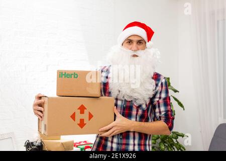 Kiev, Ucraina - 16 dicembre 2020 : Babbo Natale con scatole regalo con il marchio logo iHerb Foto Stock