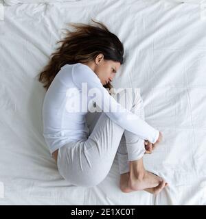 Vista dall'alto donna depressa che si aggira sulle ginocchia, sdraiata sul letto da sola Foto Stock