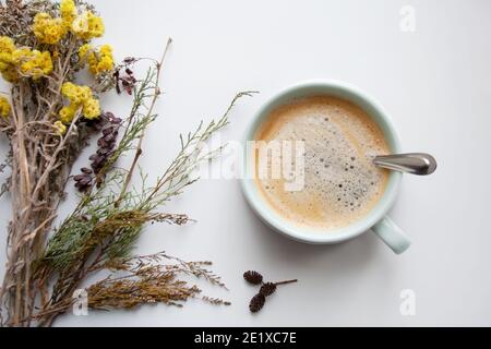 Bouquet di fiori di campo vicino a una tazza di turchese con bevanda calda al caffè su sfondo bianco da una vista ad angolo alto Foto Stock