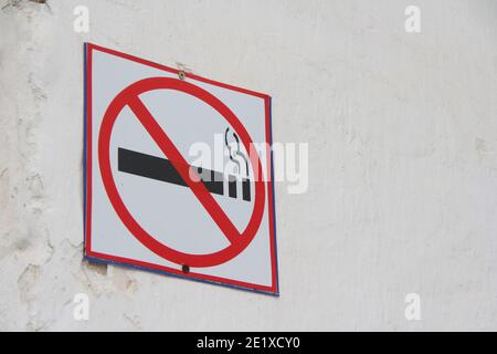 Cartello di divieto di fumo su parete bianca, concetto di assistenza sanitaria, cessazione del fumo. Fumare una sigaretta in un cerchio rosso barrato. Foto di scorta con spazio vuoto Foto Stock