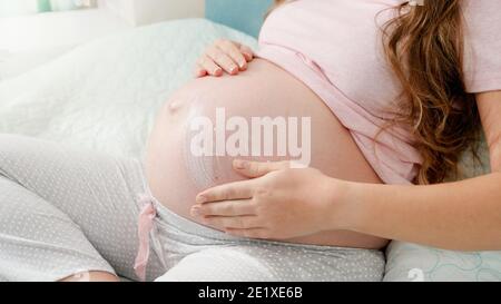 Closeup di donna incinta che applica crema idratante contro segni di stiramento sul pancia grande. Concetto di attesa bambino, gravidanza e assistenza sanitaria. Foto Stock