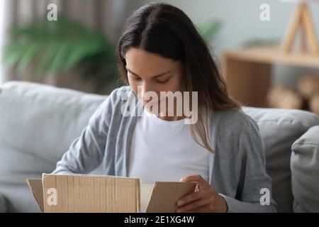 Primo piano donna curiosa che sbirciava in scatola di cartone, pacco ricevuto Foto Stock