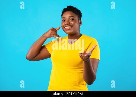 Plus-Size African Woman gesturing Chiamami su sfondo blu Foto Stock