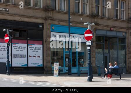 Huddersfield, Regno Unito - Luglio 12 2020: Una coppia in Huddersfield siede di fronte ai segnali di allontanamento sociale dal kirklees council. Foto Stock