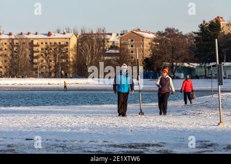 Coppia di mezza età con una passeggiata sulla spiaggia innevata di Hietaranta in una soleggiata giornata invernale a Helsinki, Finlandia Foto Stock