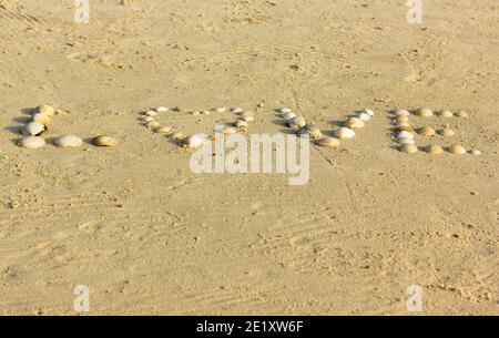 Parola amore scritto sulla sabbia con conchiglie al tramonto sulla spiaggia. San Valentino, concetto di luna di miele Foto Stock