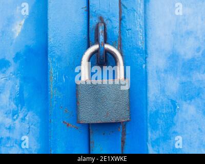 Lucchetto temprato appeso ad occhiello su una porta in metallo industriale blu. Vintage doppia porta ali in garage fila. Foto Stock