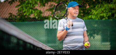 Ritratto di un uomo anziano attivo che gioca a tennis all'esterno, in forma di pensionato Foto Stock