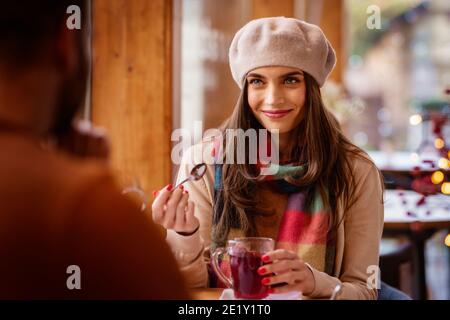 Ritratto di bella donna che indossa cappello e sciarpa mentre si siede a tavola e beve il tè nel caffè. Foto Stock