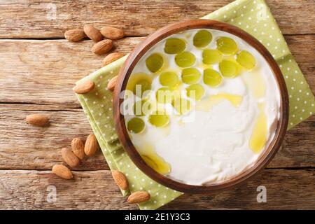 Zuppa spagnola fredda a base di mandorle tritate, pane e aglio serviti con uve verdi da vicino in una ciotola sul tavolo. Vista dall'alto orizzontale Foto Stock