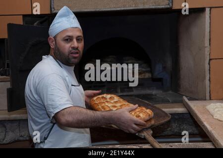 Produzione giornaliera di pane cotto con forno a legna con tradizionale Method.A panettiere che fa pita turco bread.Baker prendendo pita turco fresco pane di ov Foto Stock