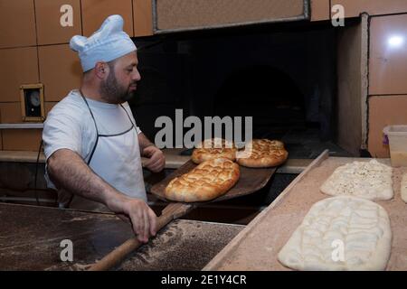 Produzione giornaliera di pane cotto con forno a legna con tradizionale Method.A panettiere che fa pita turco bread.Baker prendendo pita turco fresco pane di ov Foto Stock