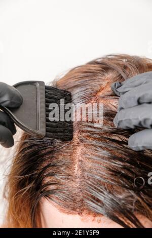 Donna che applica una tinta di colore ai capelli marroni usando una spazzola. Tintura di radici grigie di capelli a casa. Foto Stock
