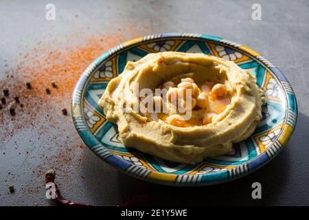 Primo piano foto di un hummus fresco fatto in casa su una colorata piastra in ceramica. Foto pasto bilanciato. Concetto di alimentazione sana. Cibo autentico del Medio Oriente. Foto Stock