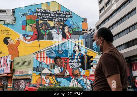 Kuala Lumpur, Malesia. 10 gennaio 2021. Un uomo che indossa una maschera facciale come precauzione contro la diffusione di Covid-19 passa oltre il murale della cooperazione economica Asia-Pacifico (APEC) a Kuala Lumpur. Credit: Faris Hadziq/SOPA Images/ZUMA Wire/Alamy Live News Foto Stock