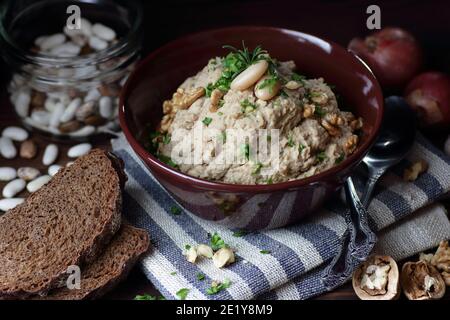 Pasta di fagioli o antipasto con noce e cipolla fritta in una ciotola su tessuto di lino su sfondo nero scuro moody, closeup, copy space, vegan e l Foto Stock