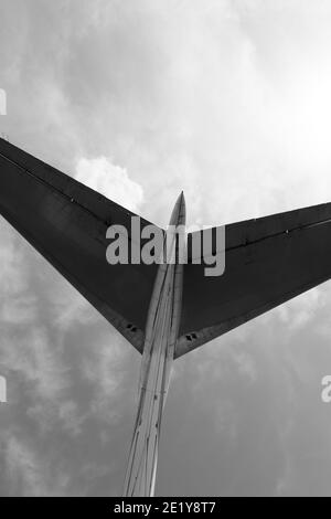 Parte della coda dell'aereo e cielo illuminato dal sole con nuvole sullo sfondo. Vista dal basso. Immagine in bianco e nero. Foto Stock