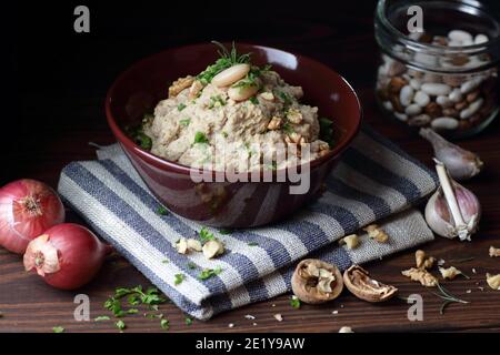 Pasta di fagioli o antipasto con noce e cipolla fritta in una ciotola su tessuto di lino su sfondo nero scuro moody, closeup, copy space, vegan e l Foto Stock