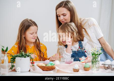 Madre amorevole che osserva le sue due figlie mentre dipingono le uova di pasqua dietro la tabella Foto Stock