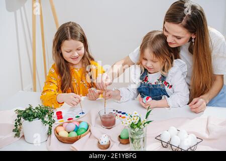 Madre amorevole osservando le sue due figlie mentre dipingono la pasqua uova Foto Stock