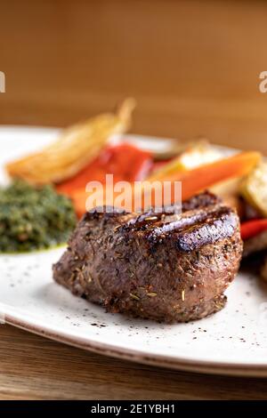 Filetto di Mignon su un piatto nero su sfondo di verdi, spezie e verdure, su un foglio di rame. Primo piano. Foto Stock