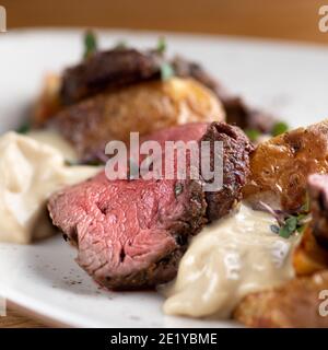 Filetto di Mignon su un piatto nero su sfondo di verdi, spezie e verdure, su un foglio di rame. Primo piano. Foto Stock