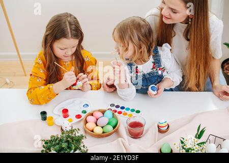 Madre amorevole che osserva le sue due figlie mentre dipingono le uova di pasqua dietro la tabella Foto Stock