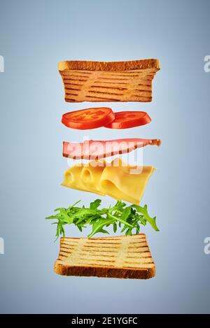 Sandwich con ingredienti volanti su sfondo blu. Concetto di cibo di mosca Foto Stock