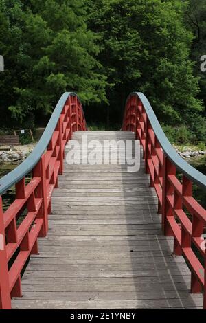 Un ponte ad arco di legno, con ringhiere laterali rosse, su un lago che conduce alla foresta a presso i Giardini Botanici Rotary a Janesville, Wisconsin, USA Foto Stock