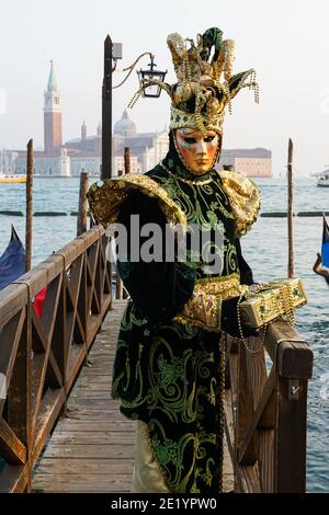 Uomo vestito in costume tradizionale decorato e maschera dipinta durante il Carnevale di Venezia con alle spalle il Monastero di San Giorgio, Venezia, Italia Foto Stock