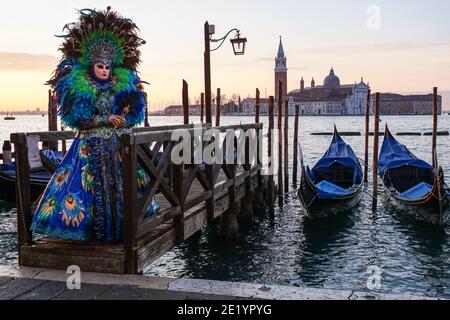 Donna vestita in costume tradizionale decorato e maschera dipinta durante il Carnevale di Venezia con alle spalle il Monastero di San Giorgio, Venezia, Italia Foto Stock