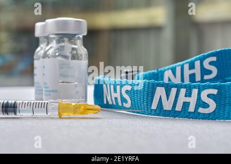 Stafford, Regno Unito - Gennaio 10 2021: Concetto di vaccino NHS. Siringa, flaconcini per iniezione e cordino NHS. Messa a fuoco selettiva. Foto Stock