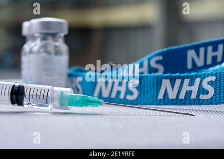 Stafford, Regno Unito - Gennaio 10 2021: Concetto di vaccino NHS. Siringa, flaconcini per iniezione e cordino NHS. Messa a fuoco selettiva. Foto Stock