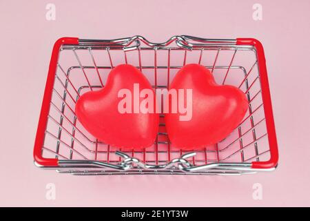 Vista dall'alto Coppia cuore rosso forma con mini carrello shopping su sfondo rosa pastello. Amore, shopping e concetto di San Valentino Foto Stock