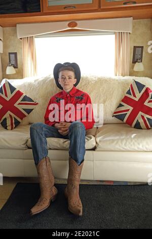 Regno Unito / Newport Pagnell /Pinders Circus / Boy in outfit occidentale seduta su divano con union jack cuscini. Foto Stock