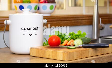 primo piano del contenitore di composto per la cucina di rifiuti alimentari riciclati con verdure tagliate e coltello su tagliere, concetto di vita sostenibile Foto Stock