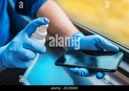 Mano di un uomo in guanti medici protettivi tiene un antisettico e spray su un telefono cellulare, fuoco morbido. Foto Stock