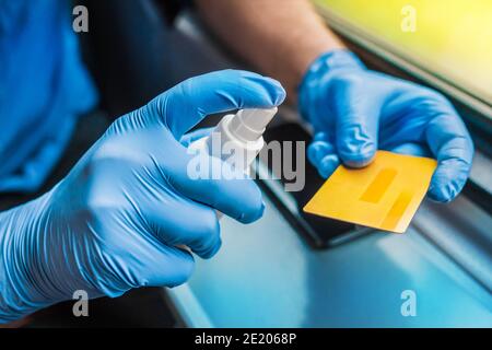 La mano dell'uomo in guanti medici protettivi tiene un antisettico e una carta di banca, primo piano. Foto Stock