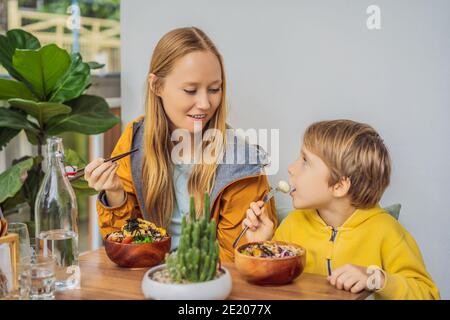 Madre e figlio mangiano il ciotola di poke organico crudo con riso e verdure primo piano sul tavolo. Vista dall'alto orizzontale Foto Stock