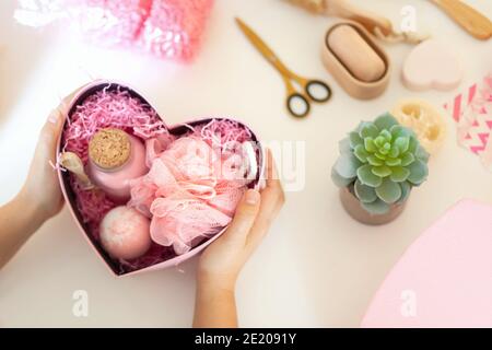 Donna che prepara scatole regalo rosa a forma di cuore con organico cosmetici naturali per la cura del corpo Foto Stock