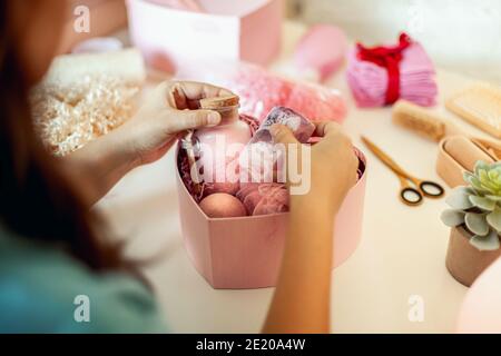 Donna che prepara scatole regalo rosa a forma di cuore con organico cosmetici naturali per la cura del corpo Foto Stock