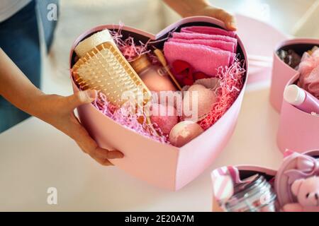 Mani donna che tengono scatole regalo a forma di cuore di colore rosa di prodotti da bagno e corpo per bridesmaids. Foto Stock