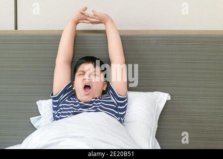 Il ragazzo grasso obeso si sveglia e si allunga sul letto al mattino, la sanità e il concetto del mondo del buon mattino Foto Stock